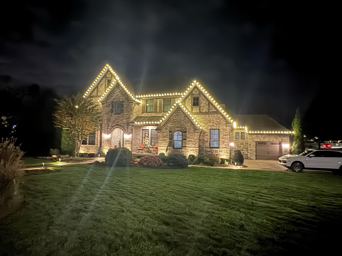 Stone and brick two-story home with warm white lights on every peak and roofline